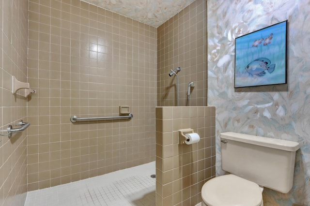 bathroom with a tile shower, toilet, and wallpapered walls