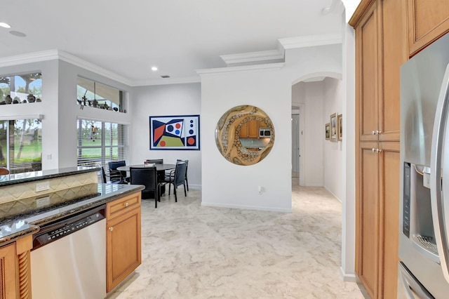 kitchen with arched walkways, stainless steel appliances, baseboards, ornamental molding, and dark stone countertops