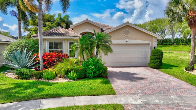 mediterranean / spanish home with an attached garage, a tile roof, decorative driveway, stucco siding, and a front lawn