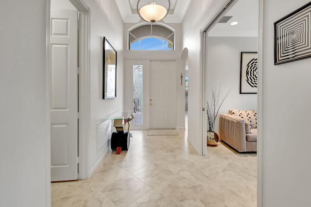 entrance foyer featuring arched walkways, baseboards, visible vents, and crown molding