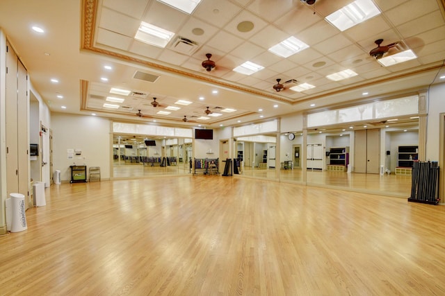 exercise room with ceiling fan, visible vents, a raised ceiling, and wood finished floors