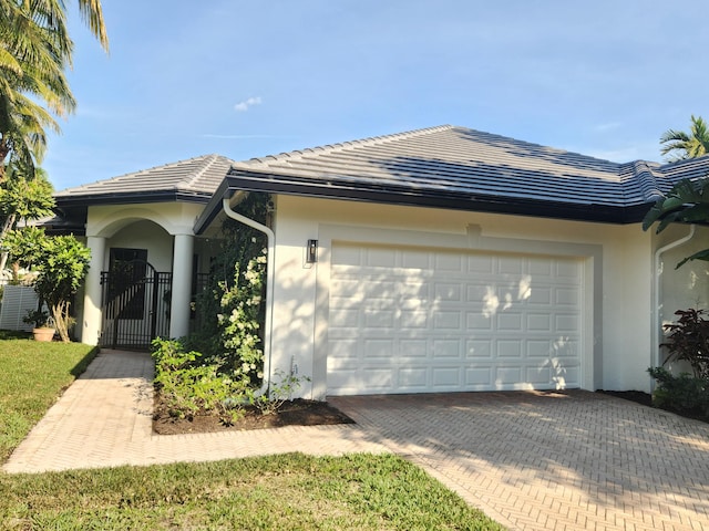 ranch-style house featuring a garage, a tiled roof, decorative driveway, a gate, and stucco siding