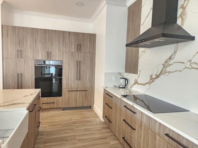 kitchen with wood finish floors, light stone countertops, ornamental molding, wall chimney range hood, and modern cabinets