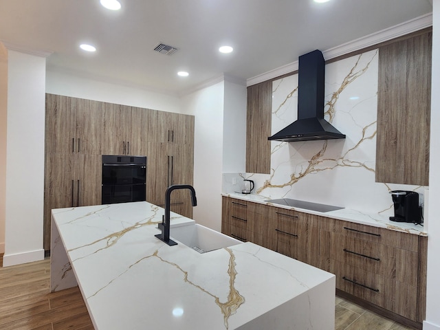 kitchen with visible vents, modern cabinets, wall chimney range hood, black appliances, and a sink