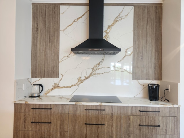 kitchen featuring black electric cooktop, light stone countertops, wall chimney exhaust hood, brown cabinetry, and modern cabinets