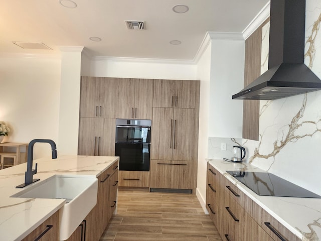 kitchen featuring light stone countertops, wall chimney range hood, modern cabinets, and a sink