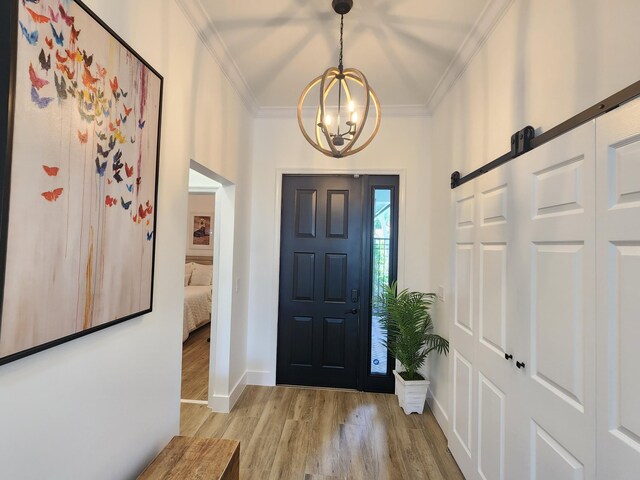 foyer featuring a barn door, an inviting chandelier, light wood-style floors, and crown molding