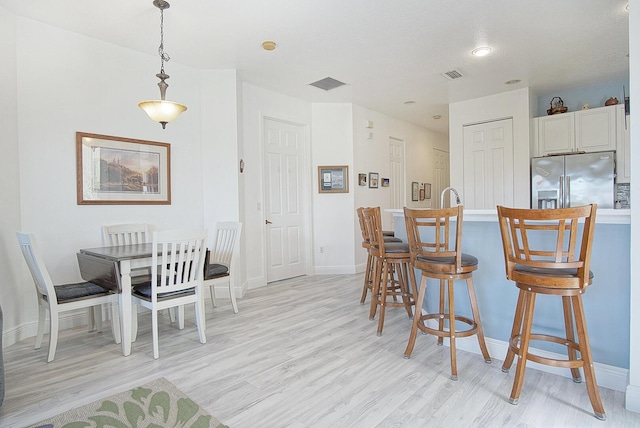 kitchen with a breakfast bar, light wood-type flooring, visible vents, and stainless steel fridge with ice dispenser