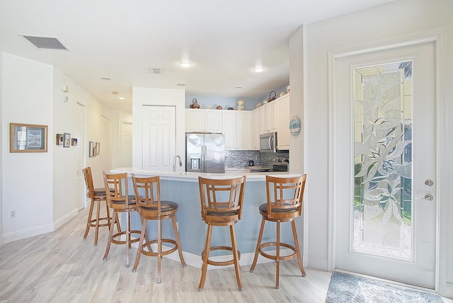 kitchen featuring a breakfast bar area, tasteful backsplash, visible vents, appliances with stainless steel finishes, and light wood-style floors