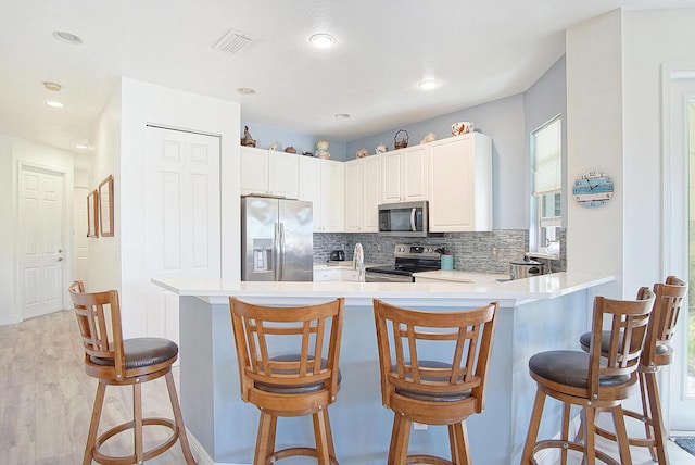 kitchen with light wood-style flooring, stainless steel appliances, a peninsula, visible vents, and backsplash