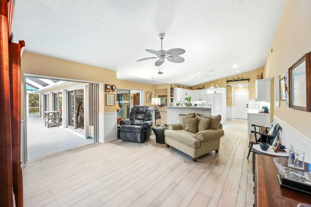 living area with vaulted ceiling, ceiling fan, light wood finished floors, and a textured ceiling