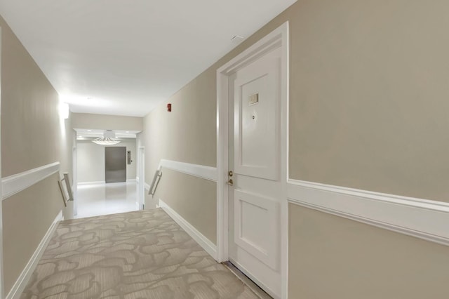 hall featuring light carpet, baseboards, and an upstairs landing