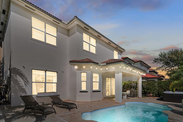 back of property at dusk with fence, a tile roof, a fenced in pool, stucco siding, and a patio area