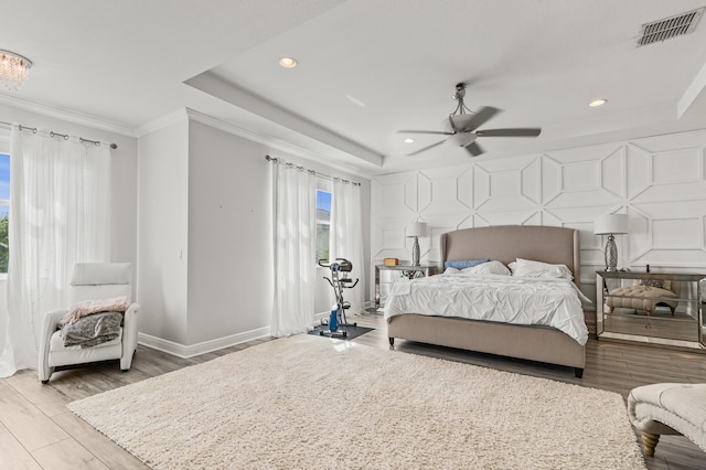 bedroom with crown molding, visible vents, an accent wall, wood finished floors, and baseboards