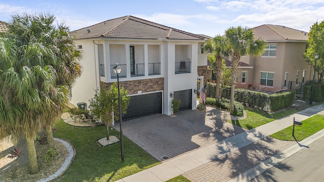 view of front of home featuring decorative driveway, stucco siding, a front yard, a balcony, and a tiled roof