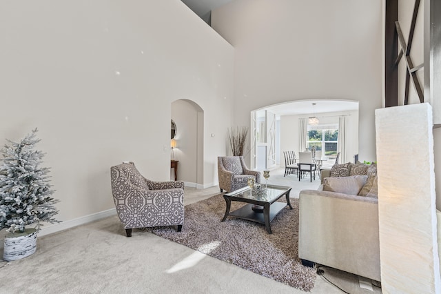 carpeted living room featuring baseboards, a high ceiling, and arched walkways