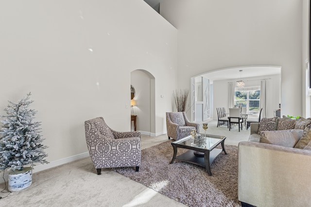 carpeted living area with arched walkways, a towering ceiling, and baseboards