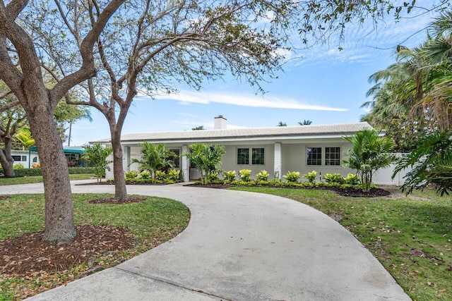 ranch-style home featuring a front lawn, curved driveway, a chimney, and stucco siding