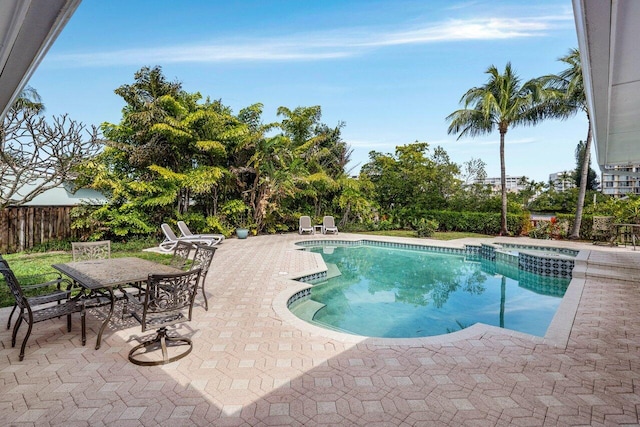 view of pool featuring outdoor dining space, a pool with connected hot tub, a patio area, and fence