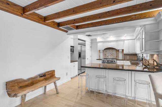 kitchen with decorative backsplash, dark countertops, appliances with stainless steel finishes, a peninsula, and beam ceiling