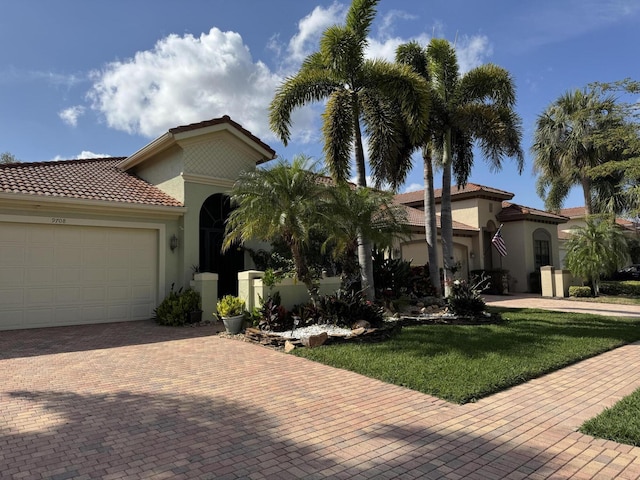 mediterranean / spanish-style house with a garage, a tiled roof, decorative driveway, a front lawn, and stucco siding