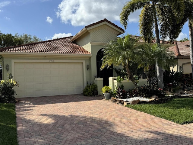 mediterranean / spanish-style home with decorative driveway, an attached garage, a tile roof, and stucco siding