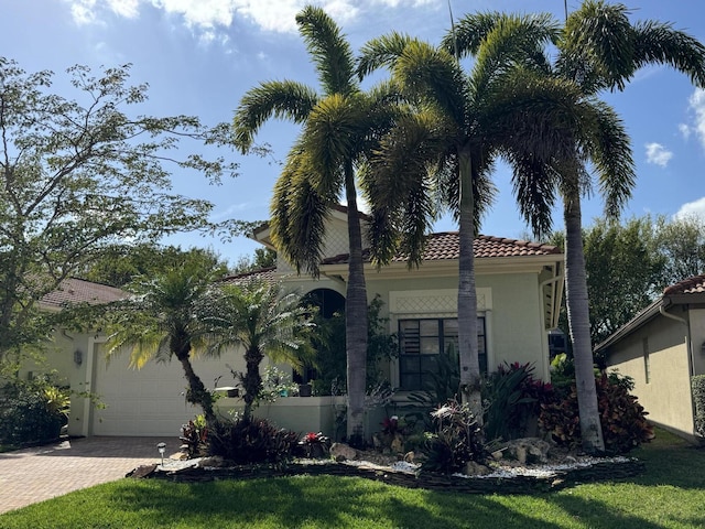 mediterranean / spanish house featuring an attached garage, a tiled roof, decorative driveway, stucco siding, and a front lawn