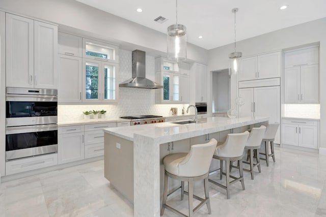 kitchen featuring stainless steel appliances, a sink, white cabinetry, visible vents, and wall chimney exhaust hood