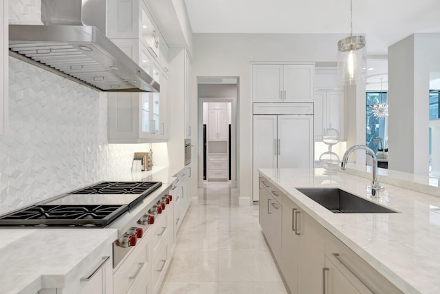 kitchen with wall chimney exhaust hood, a sink, light stone countertops, stainless steel gas cooktop, and backsplash