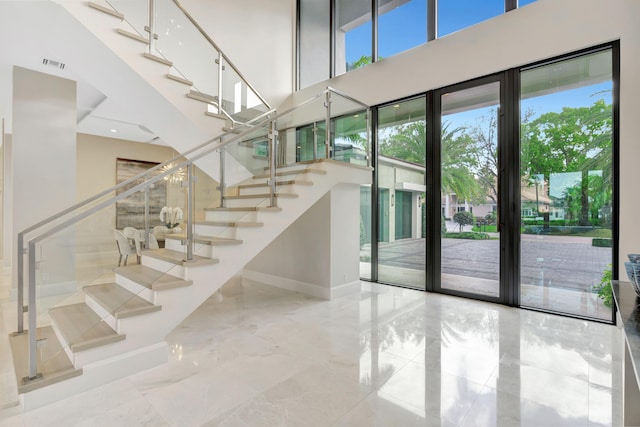 stairs featuring baseboards, visible vents, marble finish floor, and a high ceiling