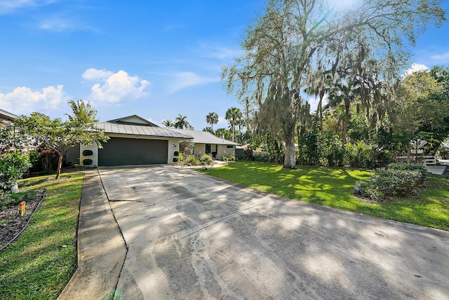 ranch-style home with driveway, an attached garage, metal roof, and a front yard