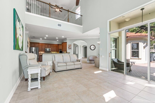 living room with arched walkways, light tile patterned floors, visible vents, baseboards, and crown molding