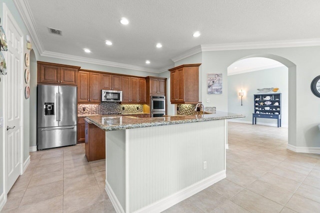 kitchen featuring light stone counters, visible vents, decorative backsplash, appliances with stainless steel finishes, and brown cabinetry