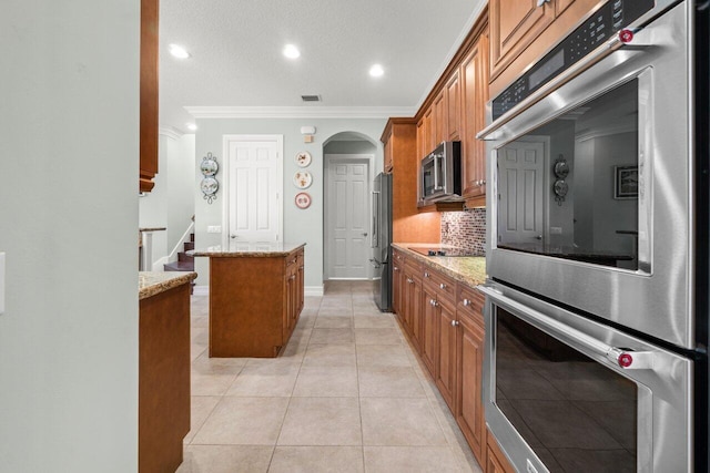 kitchen featuring light tile patterned floors, a kitchen island, appliances with stainless steel finishes, and brown cabinetry