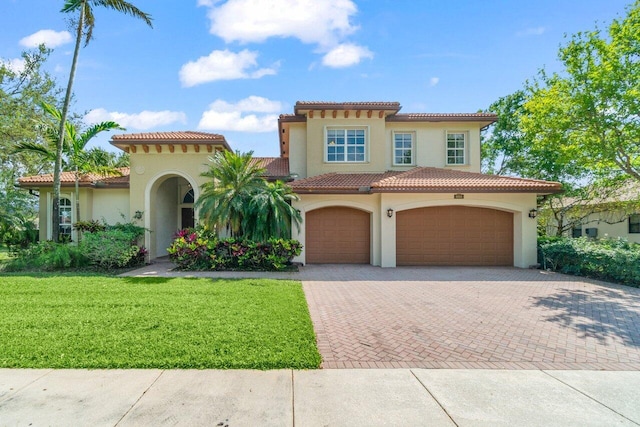 mediterranean / spanish house with decorative driveway, a tile roof, a front lawn, and stucco siding