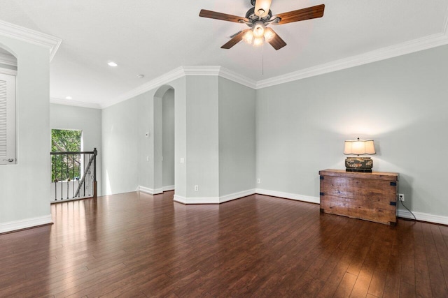 empty room featuring baseboards, arched walkways, a ceiling fan, hardwood / wood-style flooring, and ornamental molding