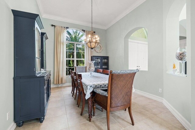 dining space with arched walkways, crown molding, light tile patterned floors, a chandelier, and baseboards