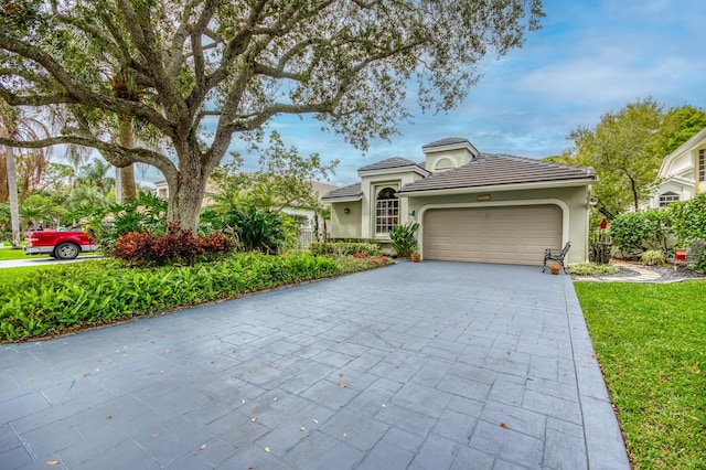 mediterranean / spanish home featuring decorative driveway, stucco siding, a garage, a tiled roof, and a front lawn