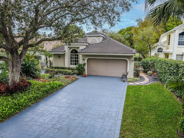 mediterranean / spanish-style house featuring decorative driveway, stucco siding, an attached garage, a front yard, and a tiled roof