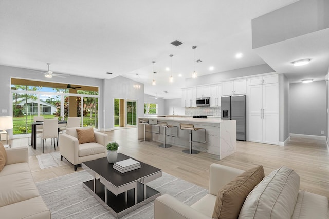 living room with vaulted ceiling, light wood finished floors, visible vents, and baseboards