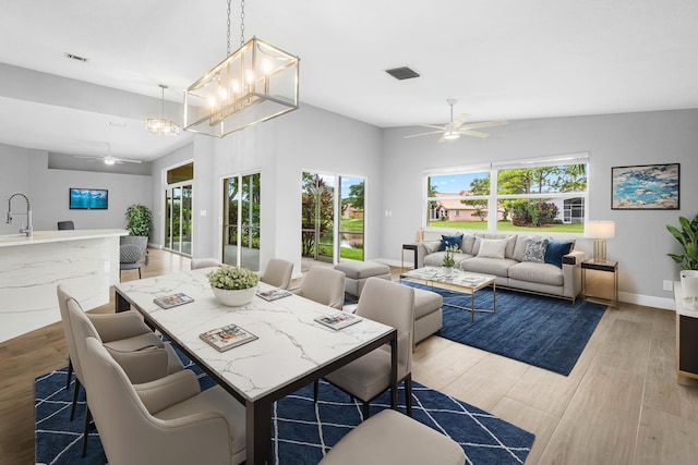 dining space with visible vents, vaulted ceiling, ceiling fan with notable chandelier, and light wood-style flooring