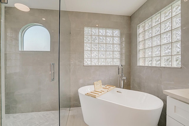 bathroom featuring a stall shower, a freestanding tub, tile walls, and vanity