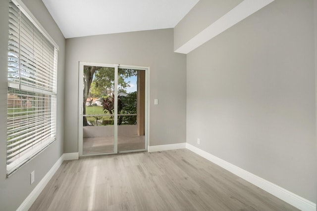 empty room with lofted ceiling, baseboards, and light wood-style floors