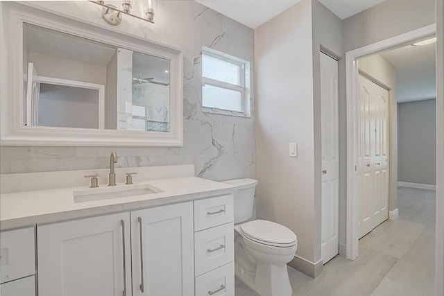 bathroom featuring baseboards, a shower, toilet, wood finished floors, and vanity