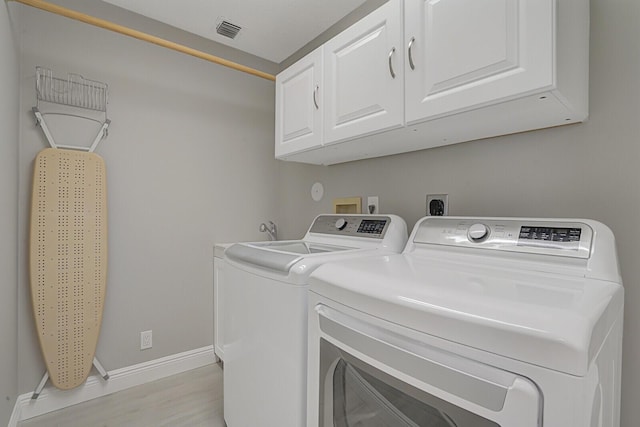 washroom featuring visible vents, cabinet space, washing machine and dryer, light wood-type flooring, and baseboards