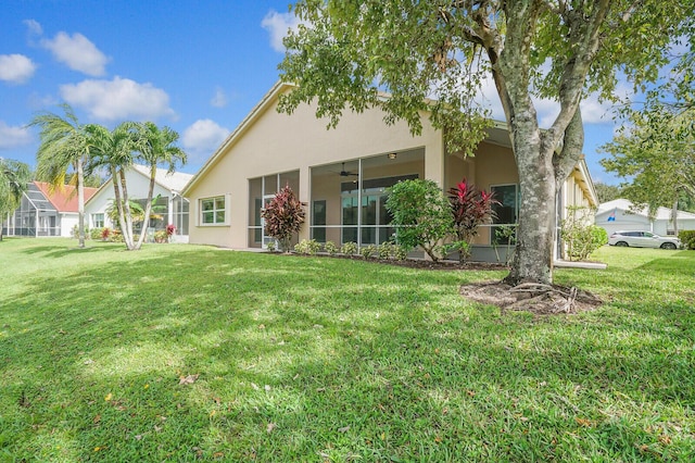 rear view of house featuring ceiling fan, a lawn, and stucco siding