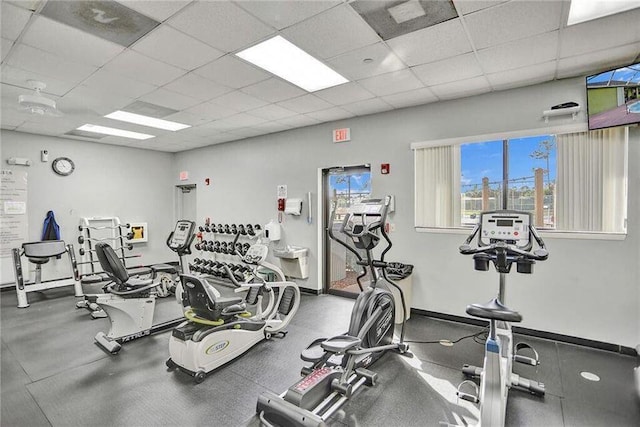 gym featuring a paneled ceiling and baseboards