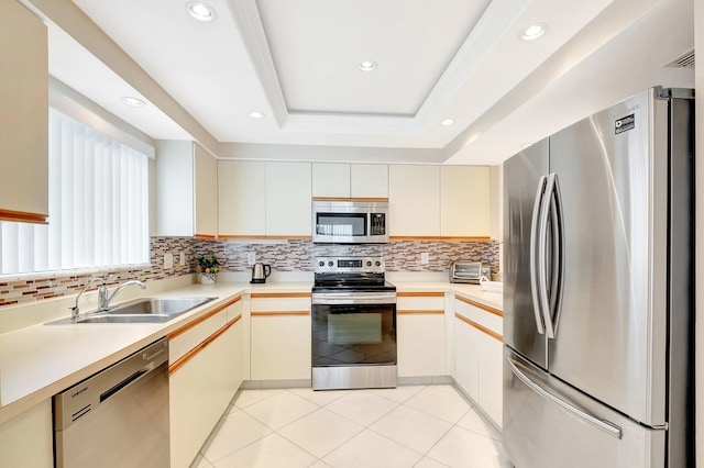 kitchen with stainless steel appliances, a sink, light countertops, a tray ceiling, and tasteful backsplash