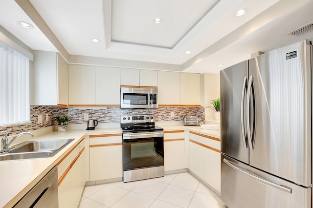 kitchen with tasteful backsplash, a raised ceiling, appliances with stainless steel finishes, light countertops, and a sink