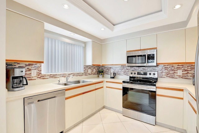 kitchen featuring light tile patterned flooring, stainless steel appliances, a sink, backsplash, and a raised ceiling